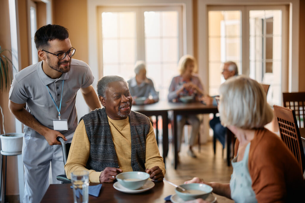 Young healthcare worker and senior people during lunch at nursing home.