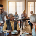 Young healthcare worker and senior people during lunch at nursing home.