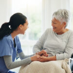 Happy woman, doctor and holding hands with senior patient in wheelchair, support or trust for healthcare at home. Medical nurse, caregiver or person with a disability smile for care or help at house