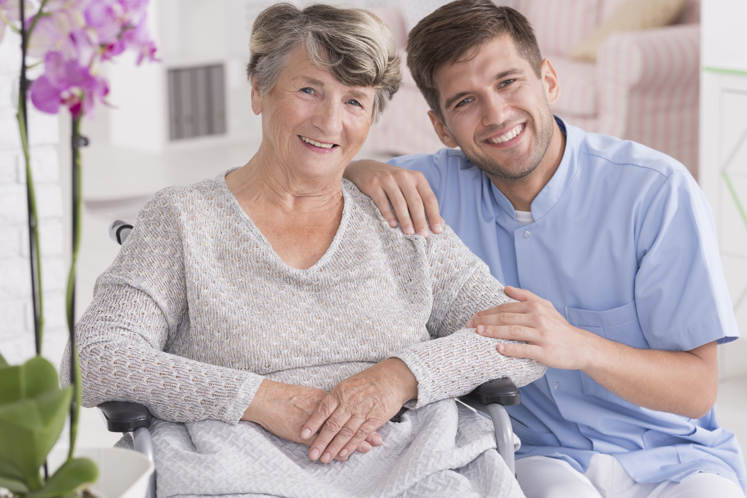 Smiling caregiver in a blue uniform providing compassionate senior home care for an elderly woman in a wheelchair. AmeriBest Home Care, trusted by families in Philadelphia, PA.